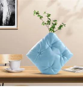 Détail d'un vase en céramique bleu clair avec un design de coussin capitonné sur une table