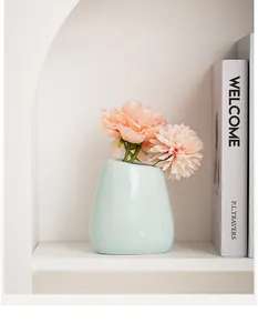 Primo piano di un moderno vaso in ceramica verde menta su una mensola bianca elegante