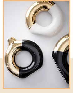 Detailed view of modern ceramic donut-shaped vases with gold and black/white glossy finish