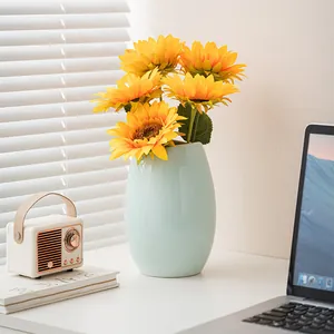 Vaso in ceramica azzurro con girasoli artificiali su tavolo bianco