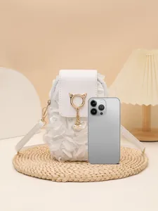 Pequeño bolso bandolera blanco con flores y colgante de gato junto a un teléfono