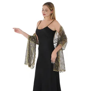 Detail view of an elegant black shawl with gold floral sequin embroidery on a model.