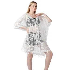 Detail van de witte kanten strand cover-up met bloemmotieven en sierlijke kwastjes