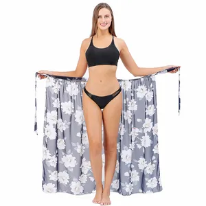 Caucasian woman wearing a grey floral print beach sarong wrap and a black bikini set