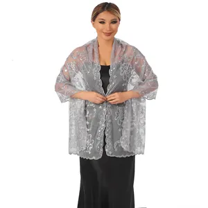 Detail view of elegant silver mesh shawl with floral sequins worn over black dress.