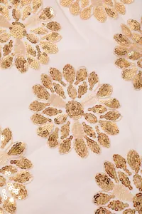 Vista macro di un elegante ricamo floreale con paillettes dorate su tulle beige