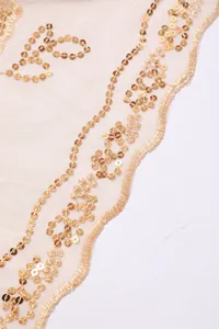 Detailaufnahme der komplizierten goldenen Paillettenstickerei auf champagnerfarbenem Mesh