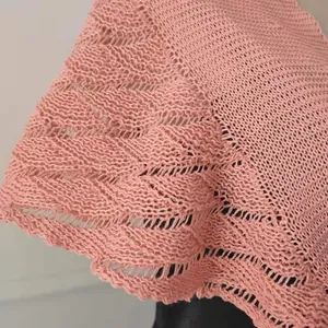 Close-up detail of a pink knit shawl showing intricate hollowed-out crochet patterns.