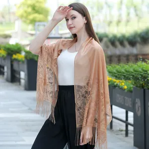 Elegant tan lace shawl with tassel fringes worn by a model in an outdoor setting