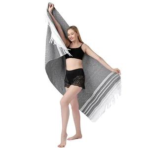 Modelo sosteniendo una gran toalla de playa turca gris con rayas blancas y flecos