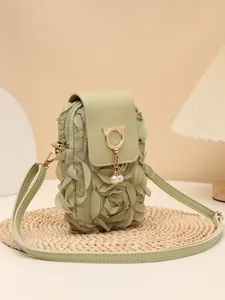 Primer plano de un bolso bandolera verde salvia con flores y colgante de gato con perlas.
