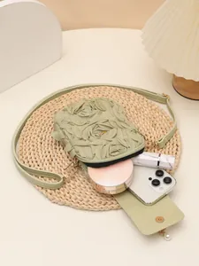 Vista detallada de la capacidad del bolso bandolera verde con pétalos de rosa y cosméticos