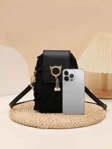 Detalle de bolso bandolera vertical con dije de gato y perla junto a un smartphone para la escala