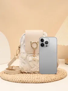 Bolso bandolera floral blanco con dije de gato junto a un teléfono inteligente para escala