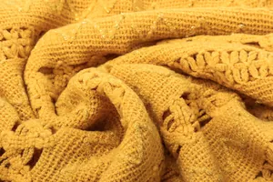 Close-up of yellow knitted fabric with shimmering gold threads and floral openwork