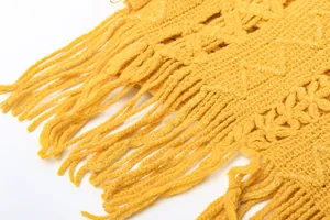 Close-up detail of yellow knitted poncho showing delicate fringe and woven texture.