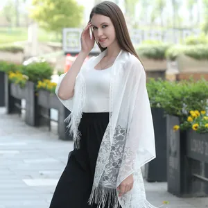 Close-up of white elegant lace shawl with floral embroidery and tassel fringe details