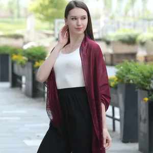 Detail view of burgundy lace shawl with fringe worn over white top and black pants