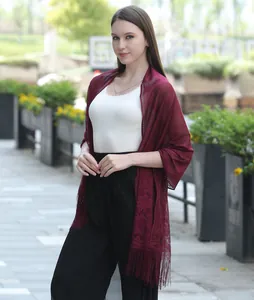 Elegant burgundy lace shawl with fringe detail shown on a model in a lifestyle setting.