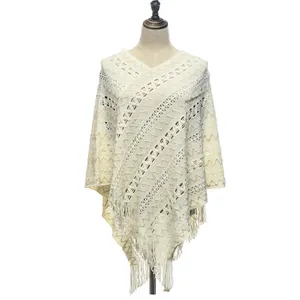 Detailed view of off-white knitted pullover poncho featuring geometric hollow pattern and tassels