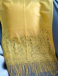 Detailed close-up view of bright yellow lace shawl featuring floral patterns and tassels