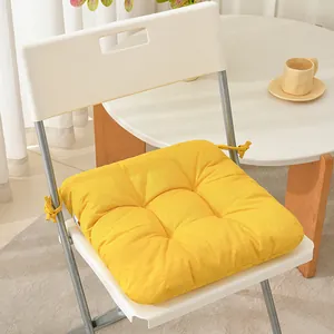 Close-up of a thick yellow fabric chair cushion with tie-back straps on a white chair.