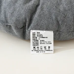 Detailansicht des weißen Pflegeetiketts auf einem grauen Leinen-Sitzkissen mit Materialinfo.