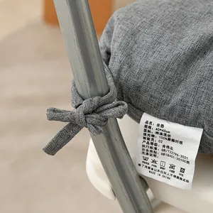 Close-up view of a grey fabric chair cushion showing the tie strap and care label tag.