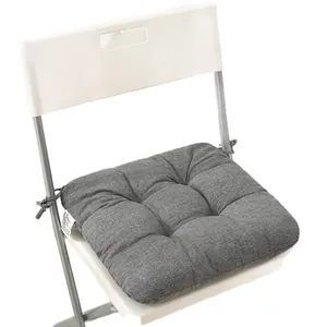 Thick tufted grey fabric chair cushion with tieback straps placed on a white folding chair