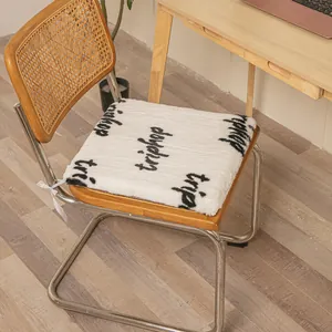 Close-up of a white plush heated seat cushion with black letters on a wooden chair.