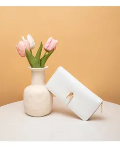 Cartera larga blanca elegante con textura de piedra y detalle dorado en fondo floral.