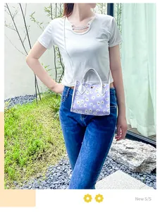 Detail view of a stylish purple small handbag with white daisy floral prints on a model