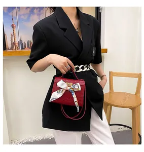 Dettaglio borsa a mano rossa con trama a pietra, foulard di seta e chiusura dorata.