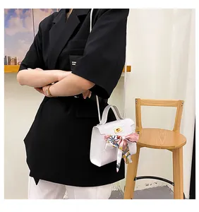 Primo piano borsa bianca effetto coccodrillo con foulard in seta e chiusura oro.