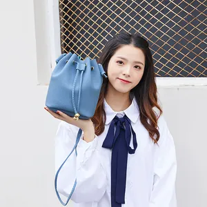 Fashionable blue lychee pattern bucket bag with drawstring closure held by model.