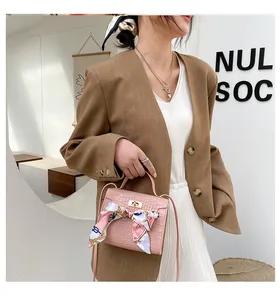 Dettaglio di una borsa rosa con trama a pietra, foulard di seta decorativo e chiusura.