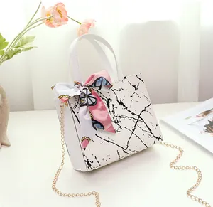 Detail view of white marble pattern handbag with decorative silk scarf and gold chain