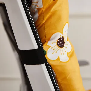 Detail of yellow floral chair cushion showing elastic strap for secure backrest fit.