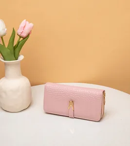 Cartera larga rosa de mujer con grabado de cocodrilo y broche dorado en la mesa