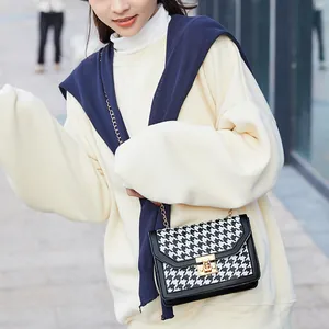 Small houndstooth crossbody bag with gold lock worn by model in outdoor setting