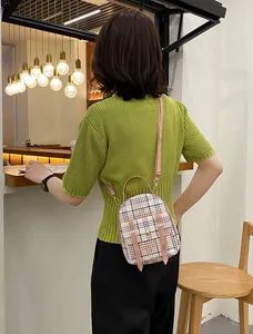 Close-up of a stylish small plaid backpack with pink straps worn as a crossbody bag