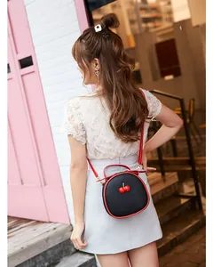 Stylish black round cherry crossbody bag with red trim worn by a model in a street setting