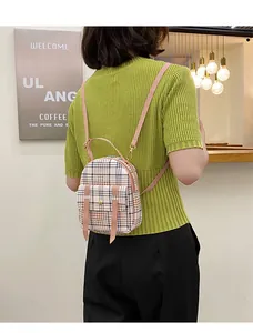Back view of a model wearing a small plaid backpack with stylish pink straps in a cafe.