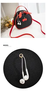 Close-up detail of black pebbled cherry crossbody bag showing the headphone cable hole