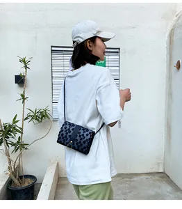Model wearing a small floral square crossbody phone bag against a white wall