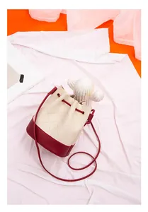 Detailed view of a quilted two-tone cream and red drawstring bucket bag on white fabric