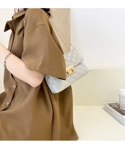 Light grey quilted crossbody bag with gold chain and lock closure worn on shoulder