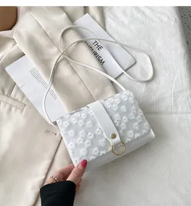 Detail view of white square crossbody bag with floral lace embroidery and gold ring