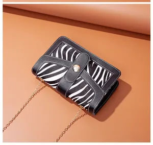 Detail of a chic zebra print crossbody bag with gold chain strap on a brown background.