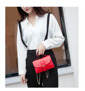 Elegant bright red croc-embossed small handbag with gold chain held by a stylish model.